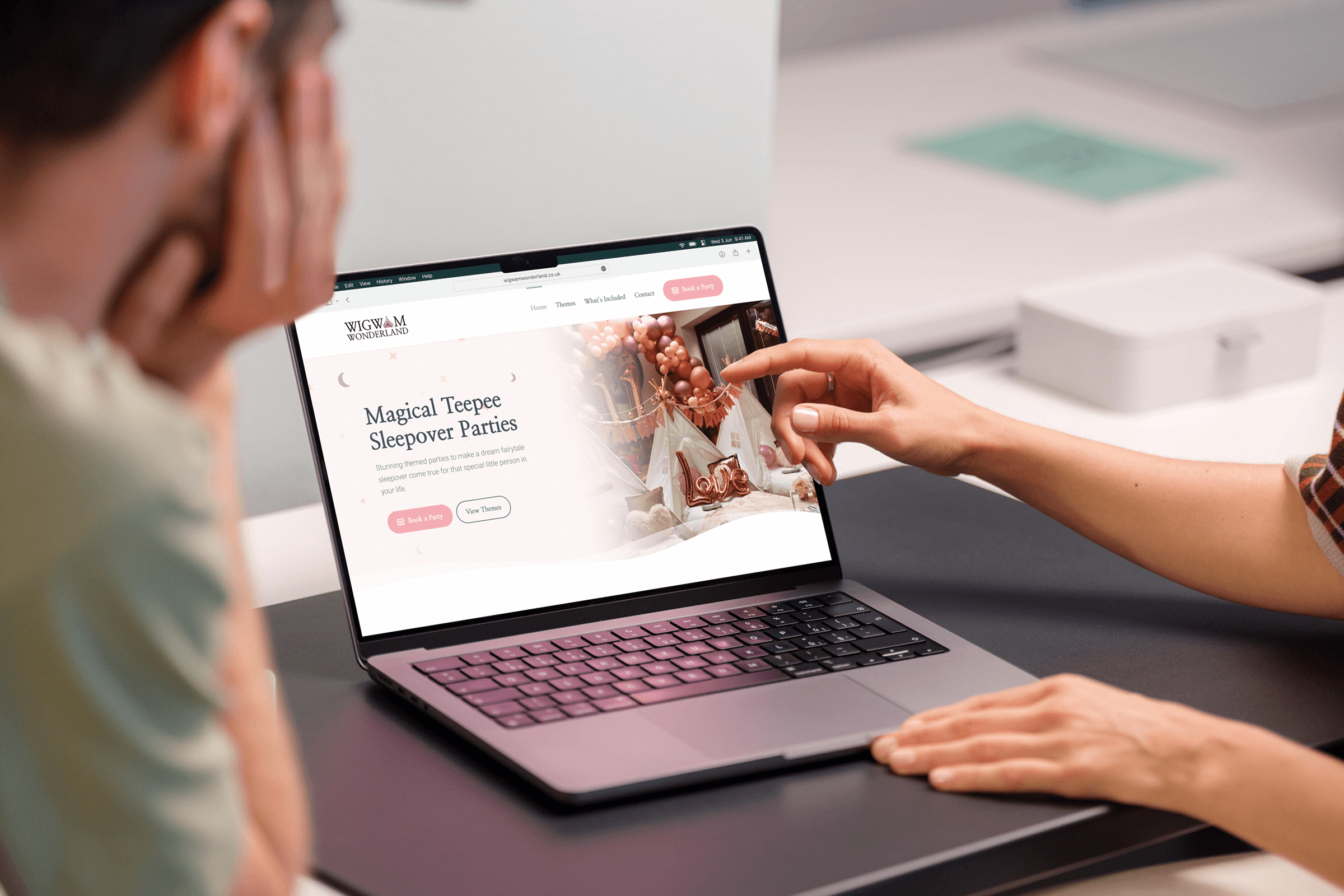 Two people reviewing a website design together on a laptop, one pointing at the homepage